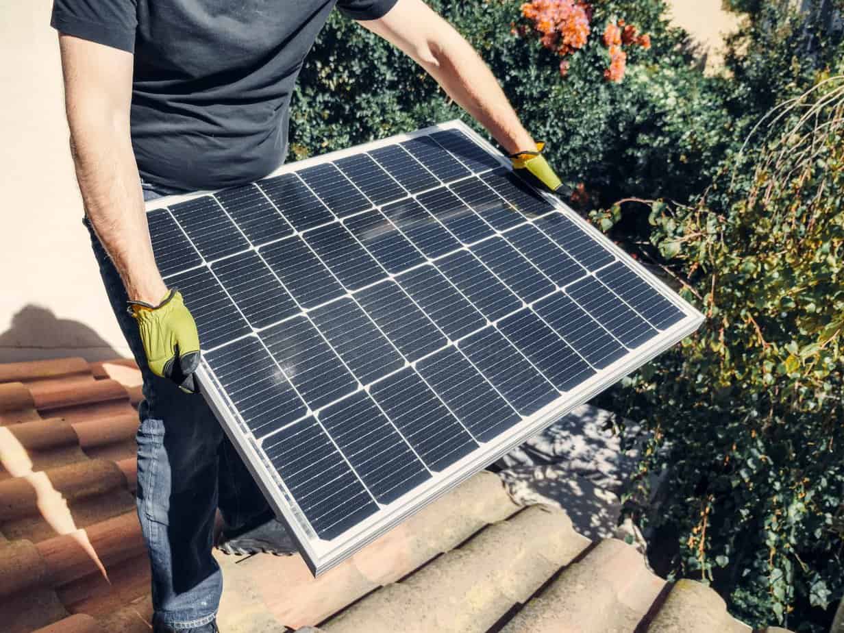 a person in black shirt holding a solar panel while standing on the roof - The Advantages and Disadvantages of Solar Energy