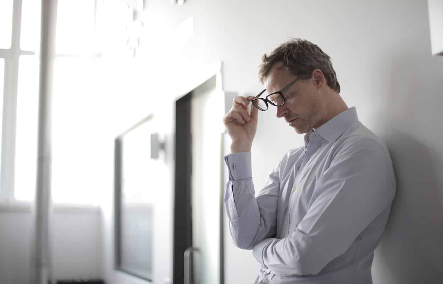 photo of man holding black eyeglasses - Stress and Tension Headaches: What causes them?