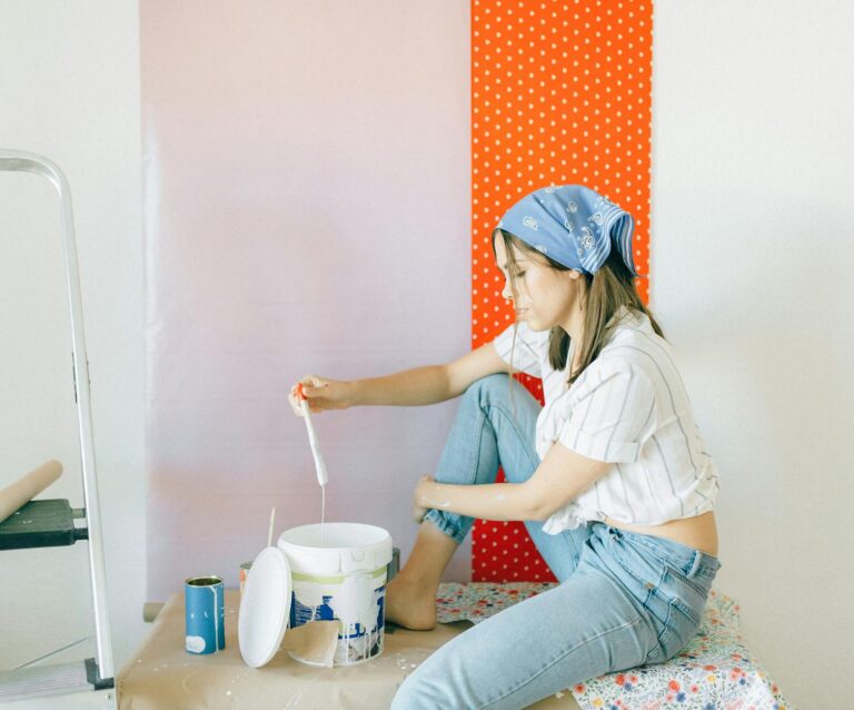 side view of a woman in striped shirt and denim jeans holding a paint brush