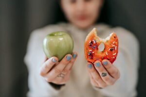 woman showing apple and bitten doughnut